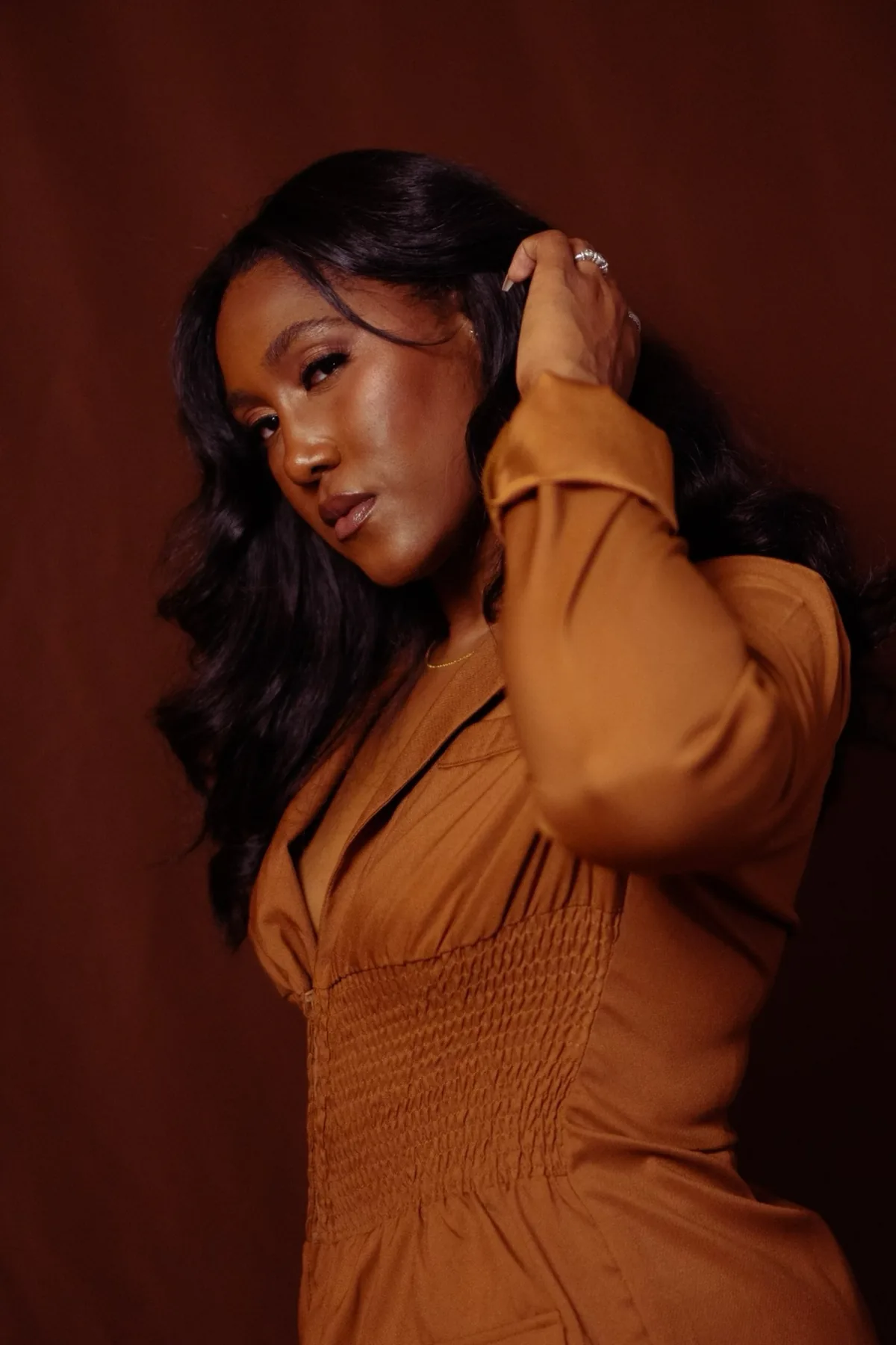 Close-up portrait of Eron Kyle, NORESTHETICS brow and lash artist, with hand raised through her hair — studio editorial shoot