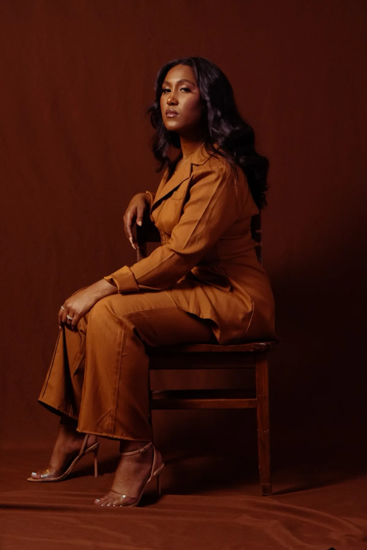 Eron Kyle, founder of NORESTHETICS, seated in a luxury studio portrait wearing a rust-colored ensemble — Fort Washington, Maryland brow and lash artist