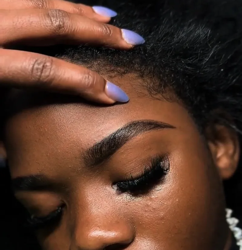 Featured brow and lash transformation by NORESTHETICS — sculpted arched brows paired with full lash extensions, hand resting in hair